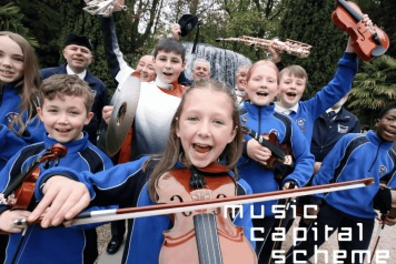 A group of young musicians celebrate holding varrious instruments in front of a fountain