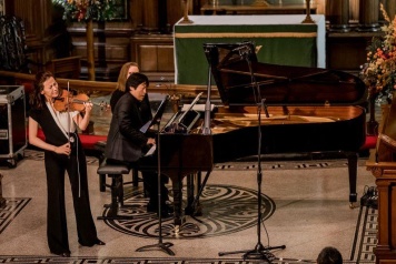 Man playing a grand piano with a women standing just ahead of him playing a violin