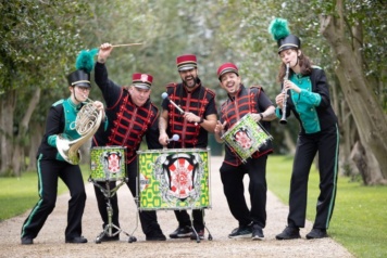 Three Drummers with their imstruments pose with two musicians dressed in black and green uniforms playing the saxophone and clarinet
