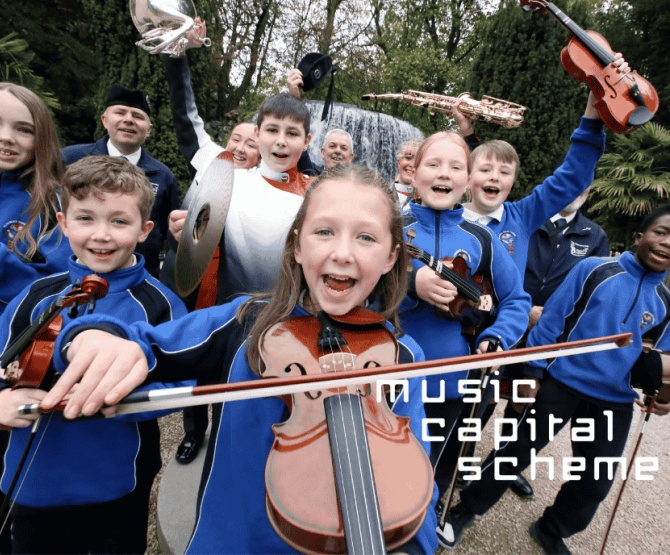 A group of young musicians celebrate holding varrious instruments in front of a fountain